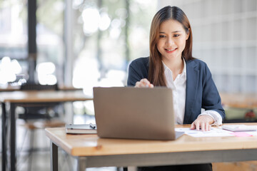 Cheerful female businesswoman entrepreneur professional working on laptop while sitting in workplace office desk, business asian woman do Documents, tax, report analysis Savings, finances economy.