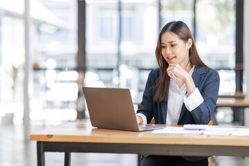 Cheerful female businesswoman entrepreneur professional working on laptop while sitting in workplace office desk, business asian woman do Documents, tax, report analysis Savings, finances economy.