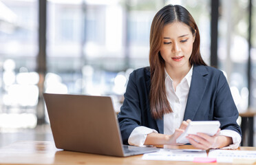 Fototapeta premium Cheerful female businesswoman entrepreneur professional working on laptop while sitting in workplace office desk, business asian woman do Documents, tax, report analysis Savings, finances economy.