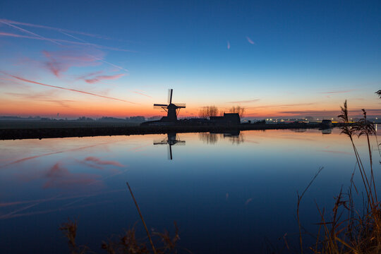 Windmill "the Adermolen" at sundown with reflection in the water on the Ringvaart canal in Abbenes, the Netherlands.