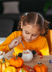 A little girl paints a clay hand made pumpkin. Halloween party. Crafts for children.