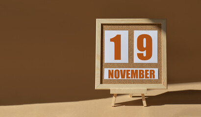 November 19th. Day 19 of month, Calendar date. Cork board, easel in sunlight on desktop. Close-up,...