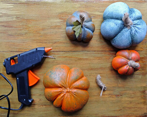 Artificial alabaster pumpkins, a hot gun and a twine tail lie on a wooden background