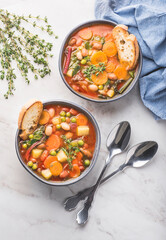 Minestrone vegetable soup on a white marble background with pieces of toasted bread and herbs. Simple  vegan rustic Italian dish, classic of Italian cuisine