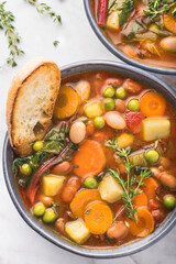 Minestrone vegetable soup on a white marble background with pieces of toasted bread and herbs. Simple  vegan rustic Italian, close-up