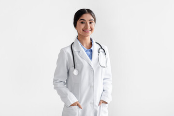Portrait of confident smiling millennial indian female doctor in white coat with stethoscope