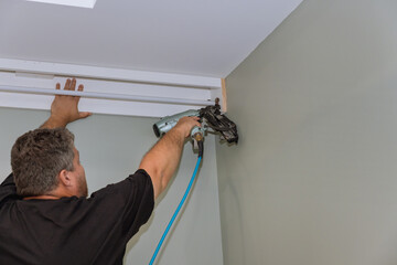 Professional handyman nailing wooden cornices on the curtain wall over window of newly constructed home. © ungvar