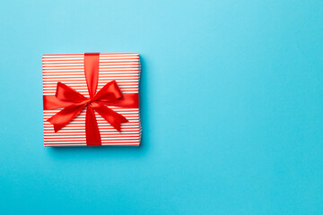 Gift box with red ribbon bow on color background, top view