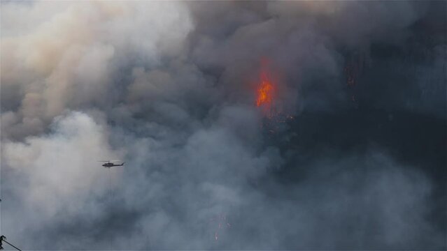 Wildfire Service Helicopter flying over BC Forest Fire and Smoke on the mountain near Hope during a hot sunny summer day. British Columbia, Canada. Natural Disaster. Slow Motion