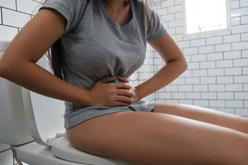 Young woman sitting on toilet and stomach ache.