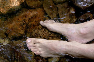 Pies de hombre sumergidos en el agua cristalina de un fresco arroyo