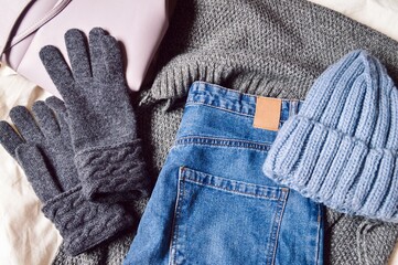 Gray woolen gloves, scarf, jeans and blue knitted hat. Flat lay winter women's outfit in casual style. Warm clothes for cold weather