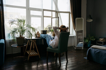 A woman is sitting at a desk in a home office and resting. There is a laptop on the table