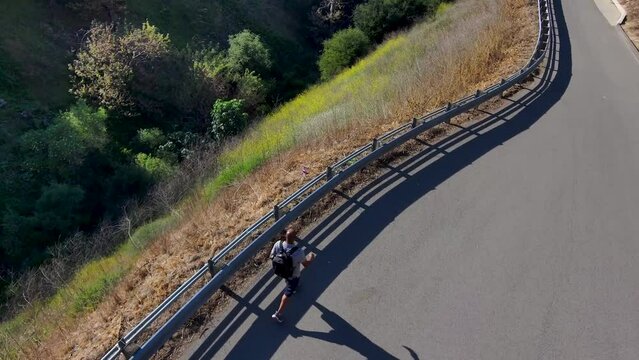 aerial footage of an African American man walking along a footpath in Malibu Creek State Park surrounded by majestic mountain ranges covered in dry brush and lush green plants in Chino Hills