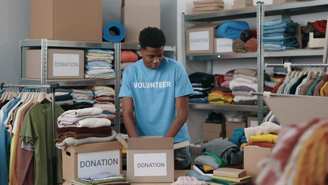 Multiracial male volunteer sorting clothes and putting it into the cupboard box at the warehouse. Humanitarian aid and donating concept. Second hand
