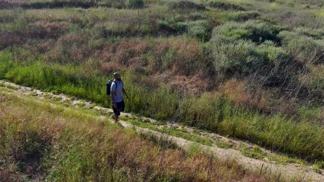 aerial footage of an African American man walking along a footpath in Malibu Creek State Park surrounded by majestic mountain ranges covered in dry brush and lush green plants in Chino Hills