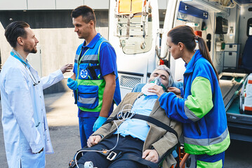 Doctor and paramedics checking health of mature male with breathing mask lying in ambulance gurney brought to hospital by EMT workers. Emergency medical services © Peakstock