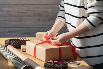 Gift wrapping in eco packaging. Young woman making bow on kraft gift box with red thread on a...