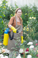 Smiling middle-aged female gardener spraying a flower bed with pesticides. Pest Control in the Garden. Blurred foreground.