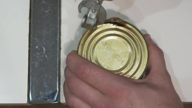 Open a can of canned food with an opener. A man opens a long-lasting food in a jar. Top view of long-term storage food in cans