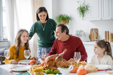 Obraz na płótnie Canvas Smiling multiethnic grandparents and grandchildren sitting near blurred thanksgiving dinner at home