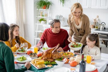 Smiling woman holding salad near daughter and family during thanksgiving dinner