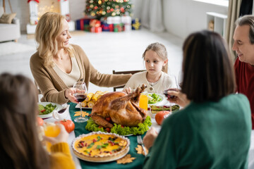 Smiling mother looking at kid near blurred family and thanksgiving dinner at home