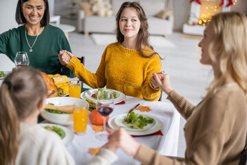 Smiling teenager holding hands of multiethnic family near thanksgiving dinner at home