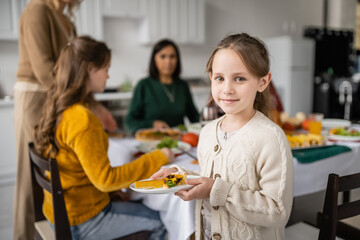 Child holding thanksgiving pie near blurred family at home
