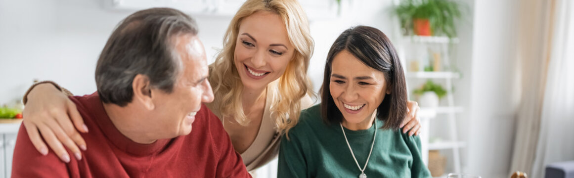 Cheerful woman hugging interracial parents during thanksgiving celebration at home, banner