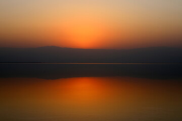 Fototapeta premium Sunrise on the shore of the Dead Sea in Israel. The sun rises from behind the mountains in Jordan.