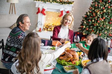 cheerful interracial family clinking glasses near delicious roasted turkey on christmas dinner at home