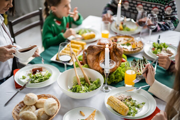 multiracial woman holding sauce boat near family having delicious thanksgiving dinner at home
