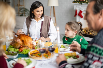 multiracial granny talking to granddaughter during christmas dinner with blurred family