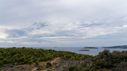 Fototapeta na wymiar Croatian Mediterranean coast photographed from a lookout mountain near Rogoznica. In the foreground forest with hiking trails, in the background the blue sea with many small islands.
