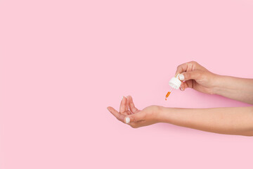 Mujer poniendose unas gotas de aceite esencial en la muñeca sobre un fondo rosa pastel. Vista de frente y de cerca. Copy space - obrazy, fototapety, plakaty