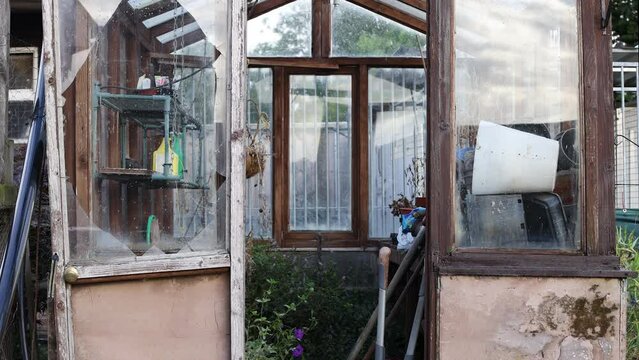 Creepy dilapidated greenhouse with smashed window and overgrown plants