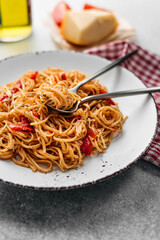 Italian pasta with tomato sauce and tomatoes, in a light plate. Nearby is a cloth napkin, a bottle of wine, cheese and cutlery