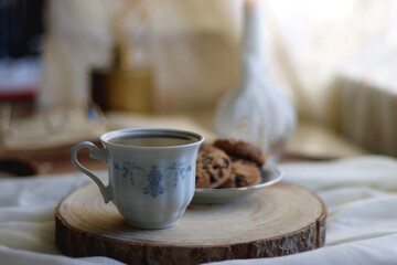 Cup of tea or coffee, plate of chocolate chip cookies, open book, reading glasses, candle and vase with flowers. Selective focus.