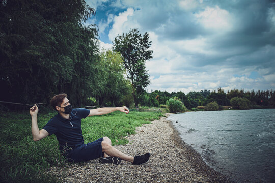 Masked guy is sitting and throwing a stone to lake