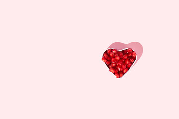 Pomegranate seeds in heart shaped bowl on pink background. Minimal red fruit concept.