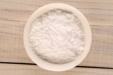 One white ceramic salt shaker with salt on a wooden table, macro, top view.