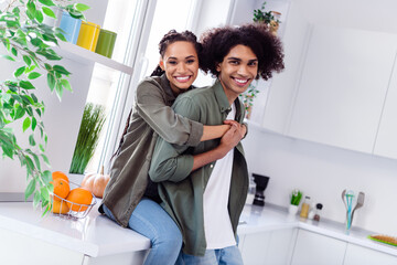 Photo of charming cheerful couple spend time together in kitchen room girlfriend hug her boyfriend behind feel comfy