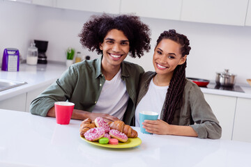 Portrait of cheerful good mood siblings enjoy weekend morning tea together eating yummy sweet doughnuts