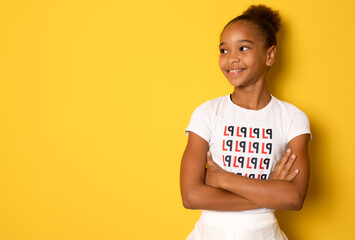 Smiling little african american girl posing with arms folded isolated over yellow background.