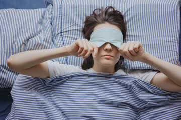 top view of a woman in bed wearing a sleep mask, a European tired woman is sleeping and...