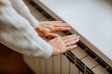 Obraz premium Woman's hands in winter sweater is touching home radiator and feeling cold
