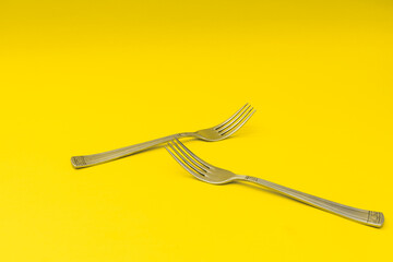 Silver forks lie on a yellow background, minimalism