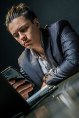 Young businessman in formal wear sitting in the office is reading a message on his smartphone that puzzles him. Business, entrepreneurship, leadership concept