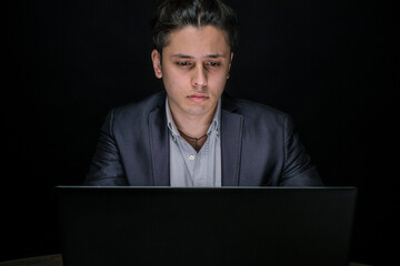 Young businessman in formal wear sitting in the office is working on the computer late into the night. Business, entrepreneurship, leadership concept